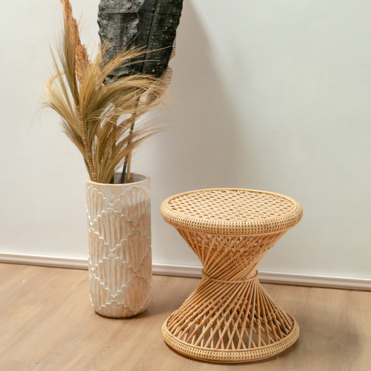 Bijzettafel van rotan staand voor een witte muur op een houten vloer