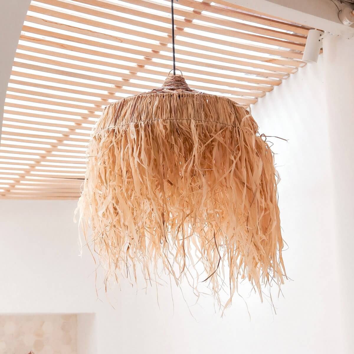 Lampenkap van raffia met lange witte franjes voor een witte muur