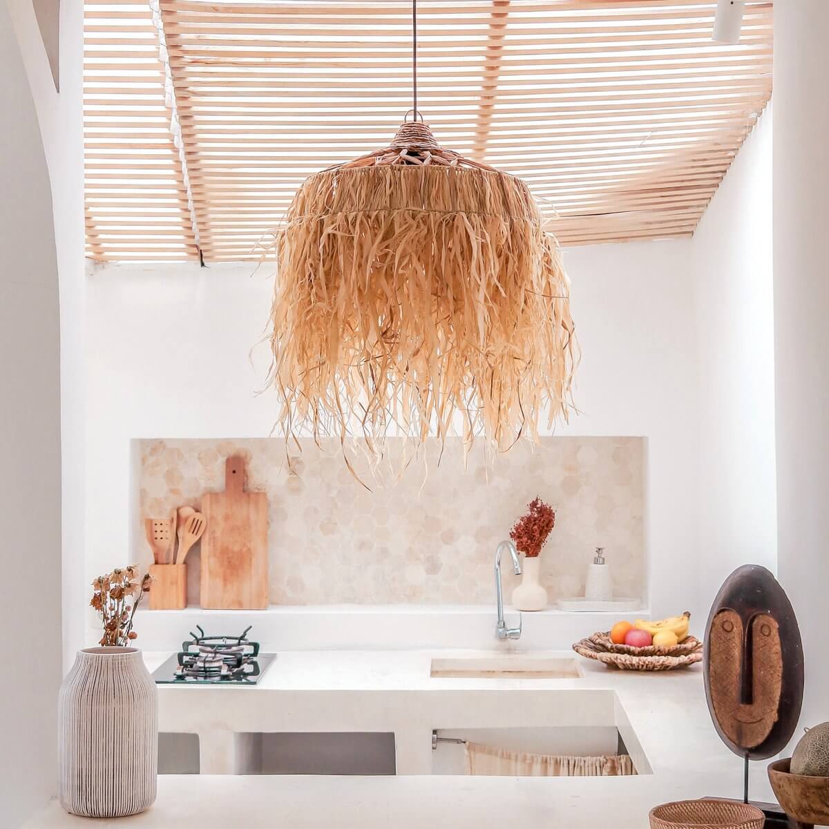 Hanglamp van raffia met lange witte franjes in een witte stenen keuken