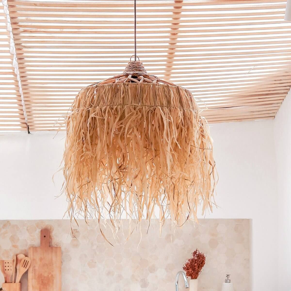 Hanglamp van raffia boven een witte stenen keuken