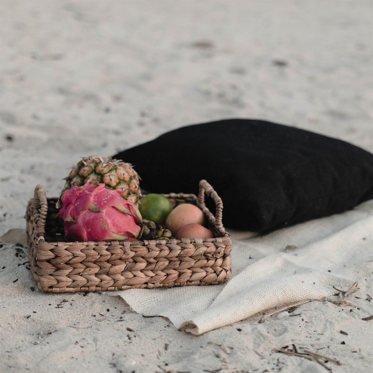 Dienblad met handvat van waterhyacint met fruit erin liggend op een doek op het strand