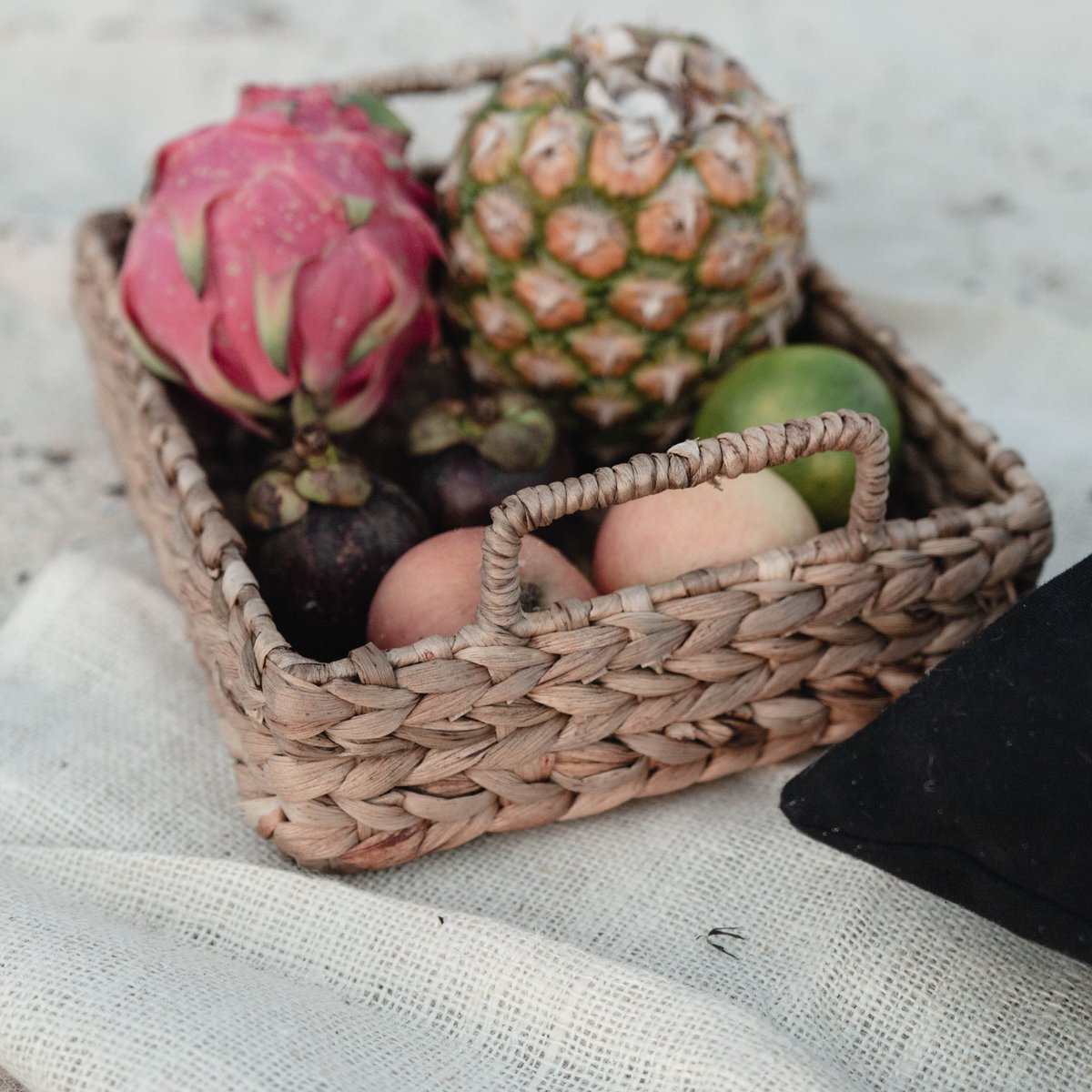 Dienblad van waterhyacint met handvat met fruit erin liggend op een doek op het strand