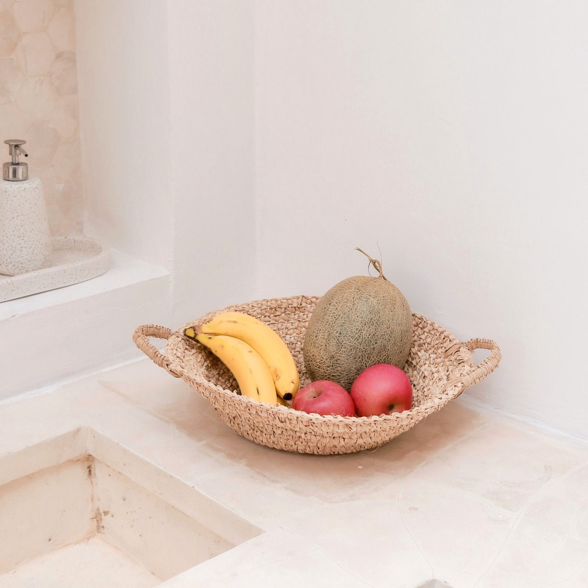 Fruitmand van raffia met fruit erin naast een gootsteen