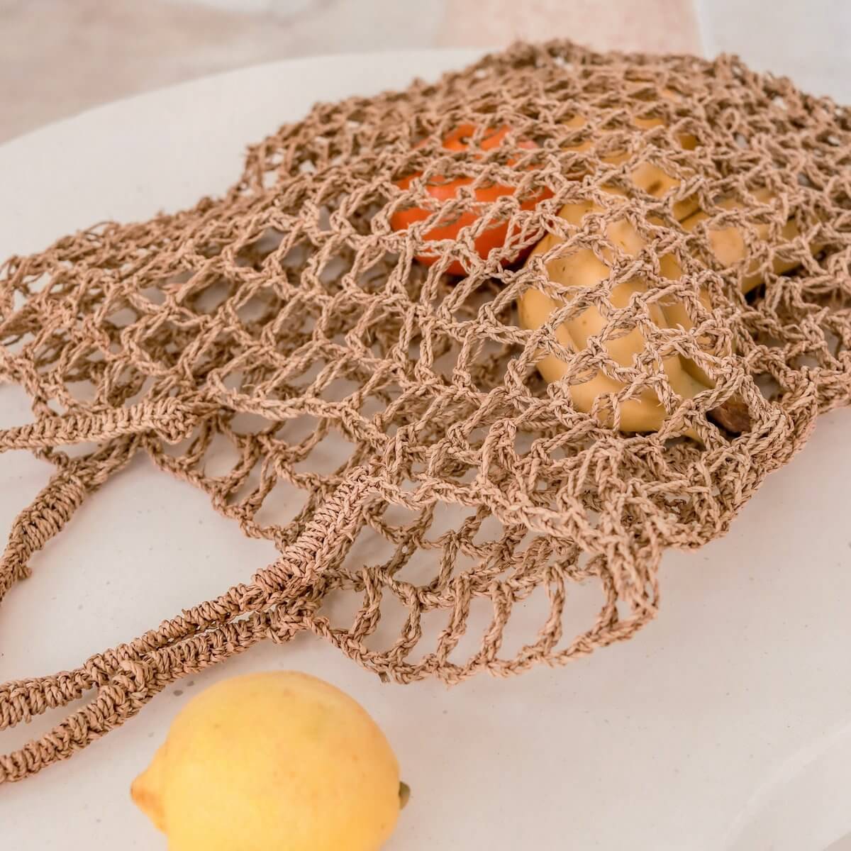 Boodschappentas van raffia koorden liggend op een tafel met fruit erin