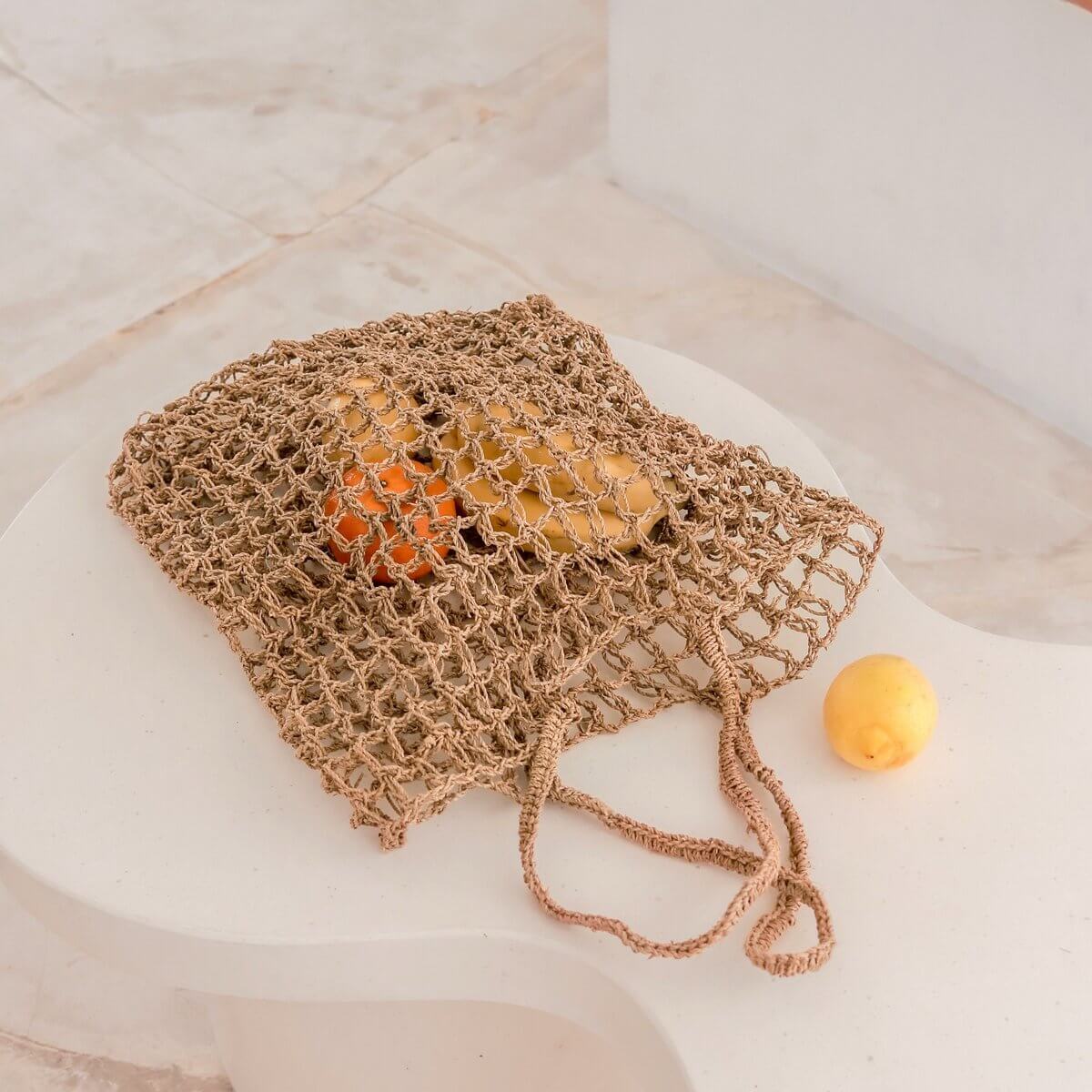 Strandtas van raffia liggend op een witte tafel met fruit erin