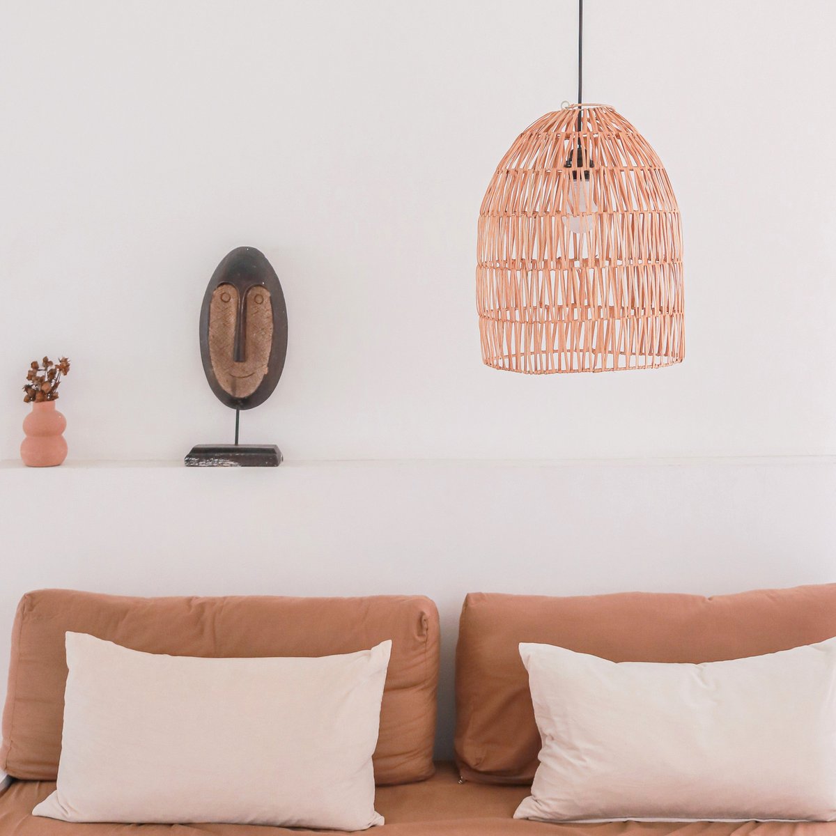 Hanglamp van rotan hangend boven een bank voor een witte muur