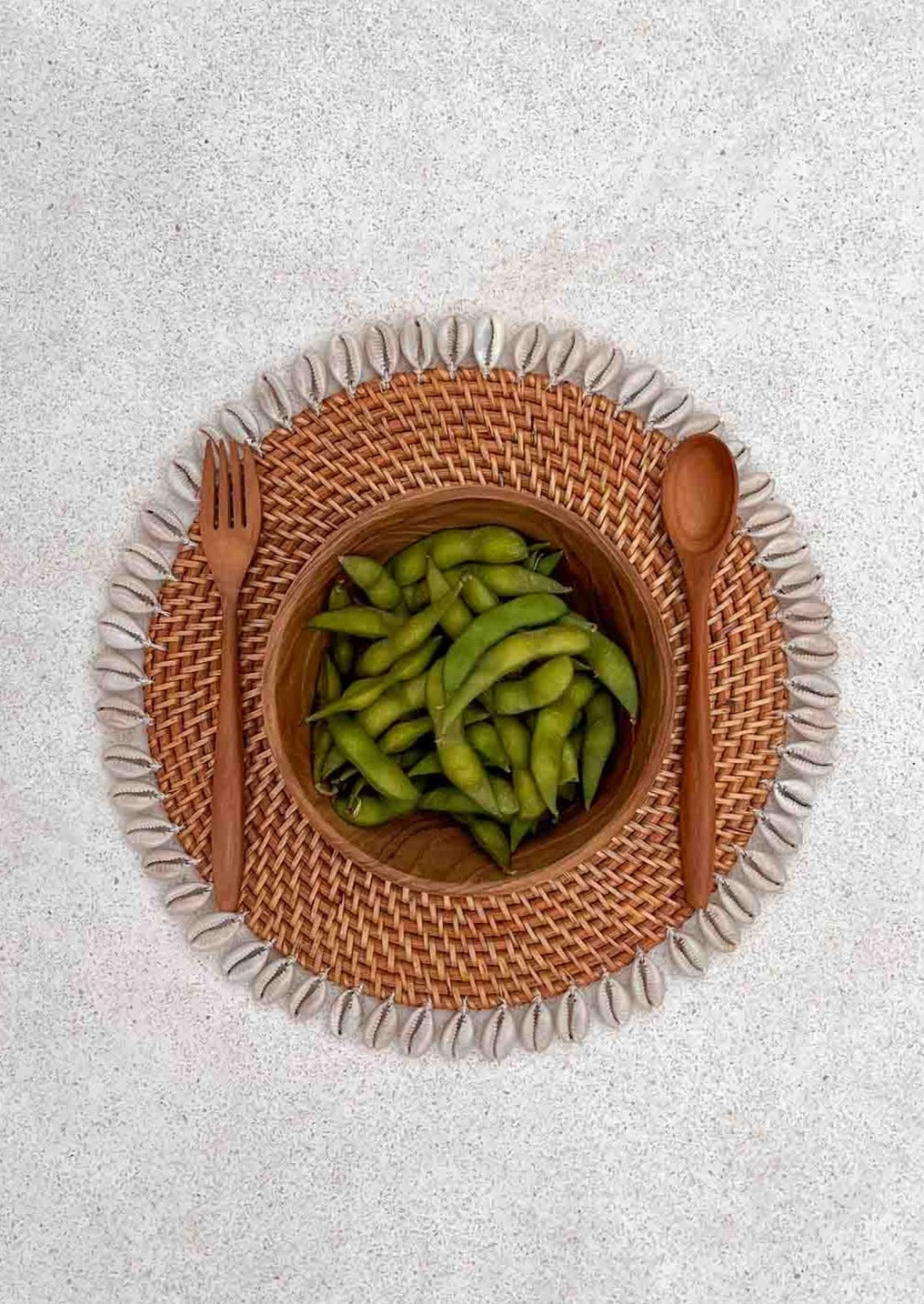 Houten bestek naast een houten kom op een schelpen placemat