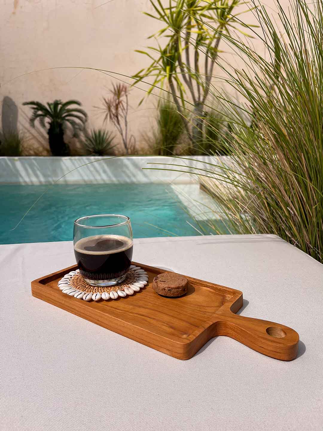 Houten borrelplank naast een zwembad met daarop een kop koffie en een koekje