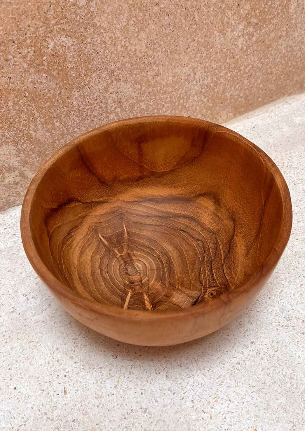 Teak houten kom gericht op de binnenkant, staand voor een muur op de grond