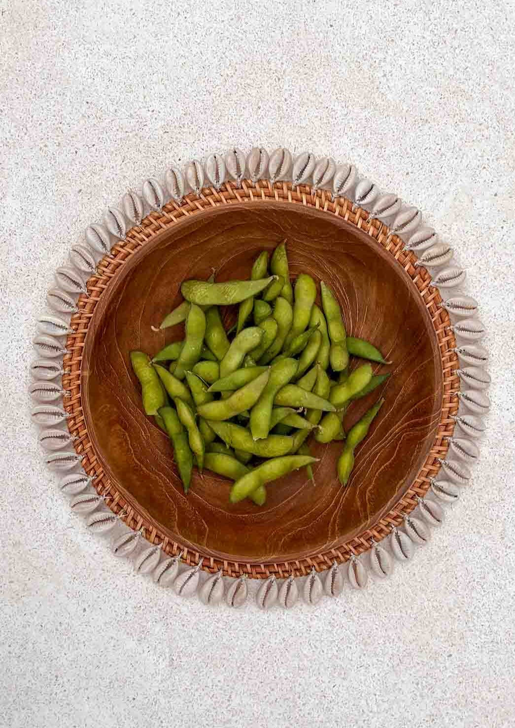 Schelpen placemat met daarop een houten kom staand op de grond