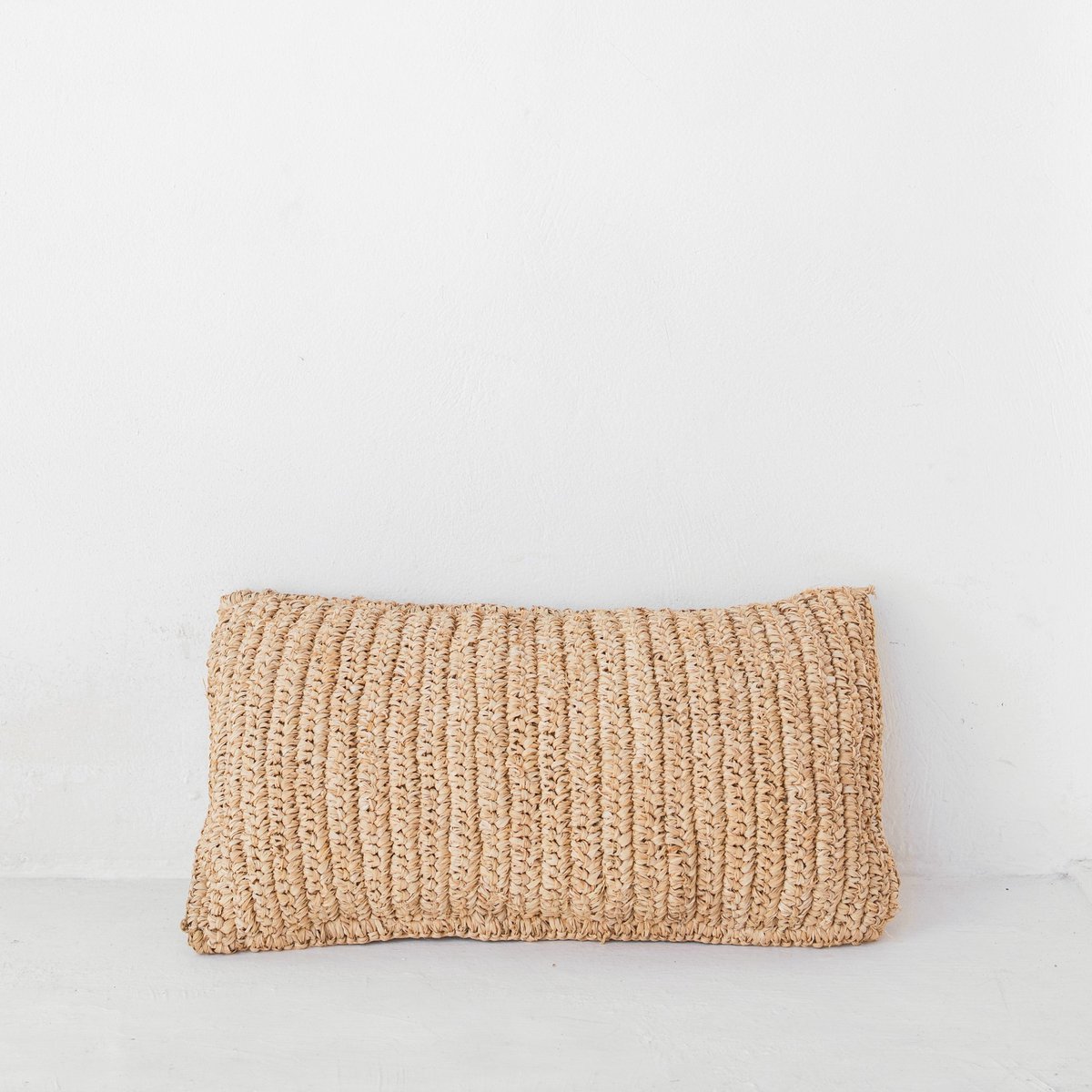 Kussen van raffia liggend tegen een witte muur
