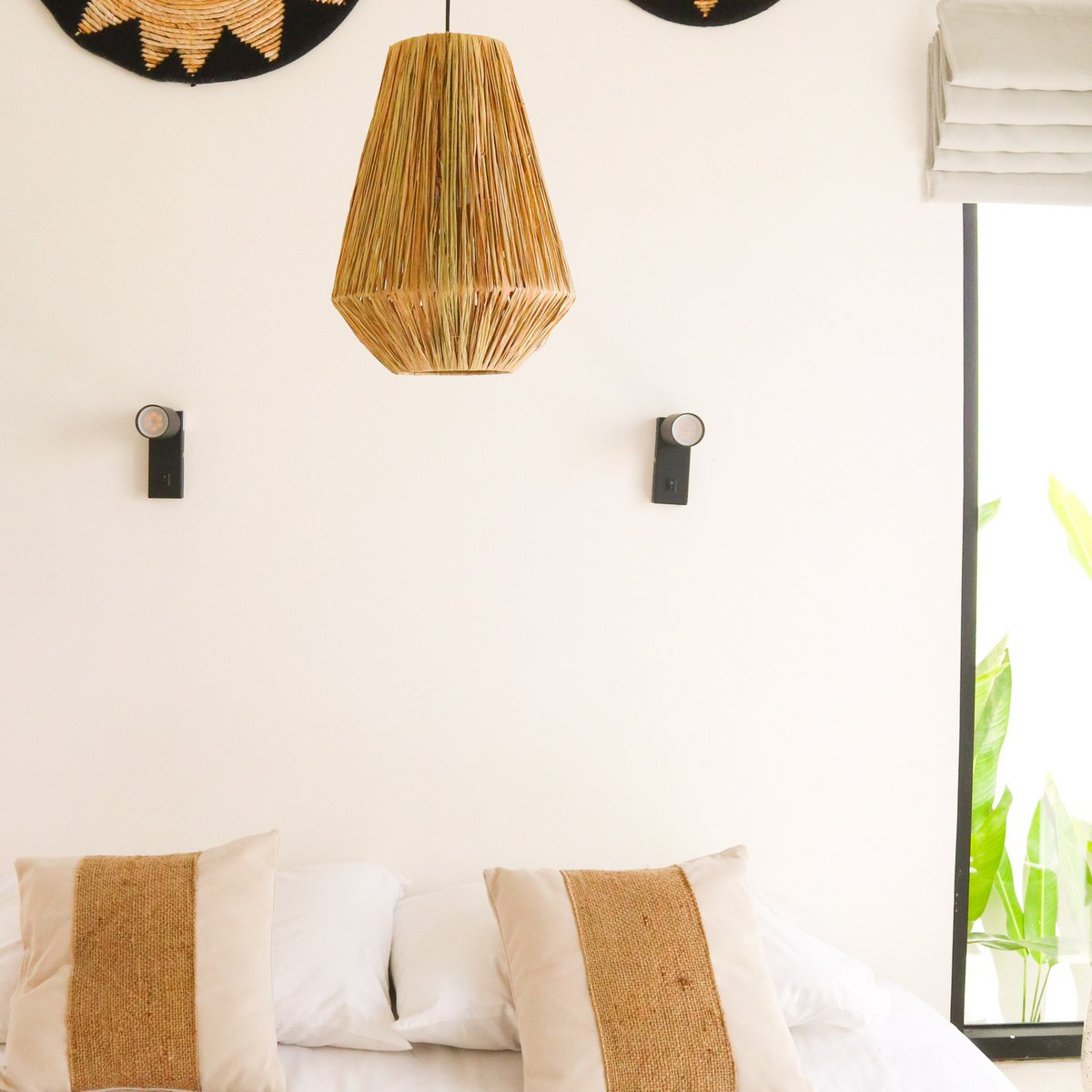 Hanglamp van raffia hangend voor een witte muur boven een bank