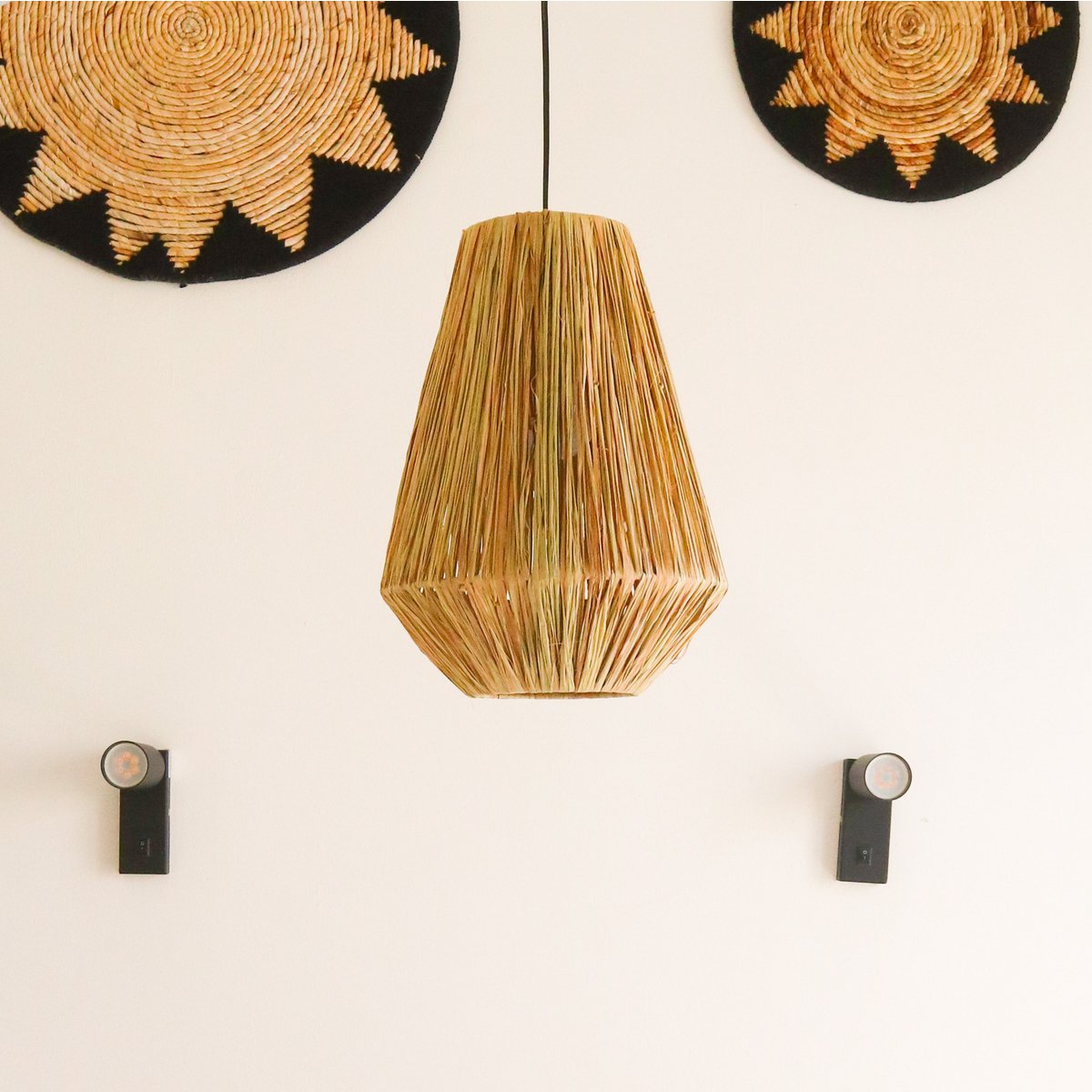 Hanglamp van raffia hangend voor een witte muur met wandschalen erop