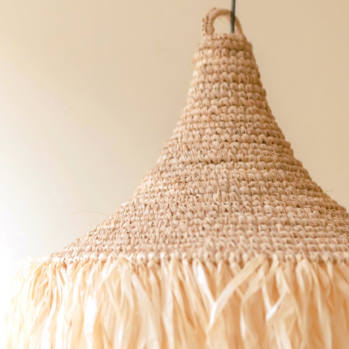 Hanglamp van raffia met franjes voor een beige muur