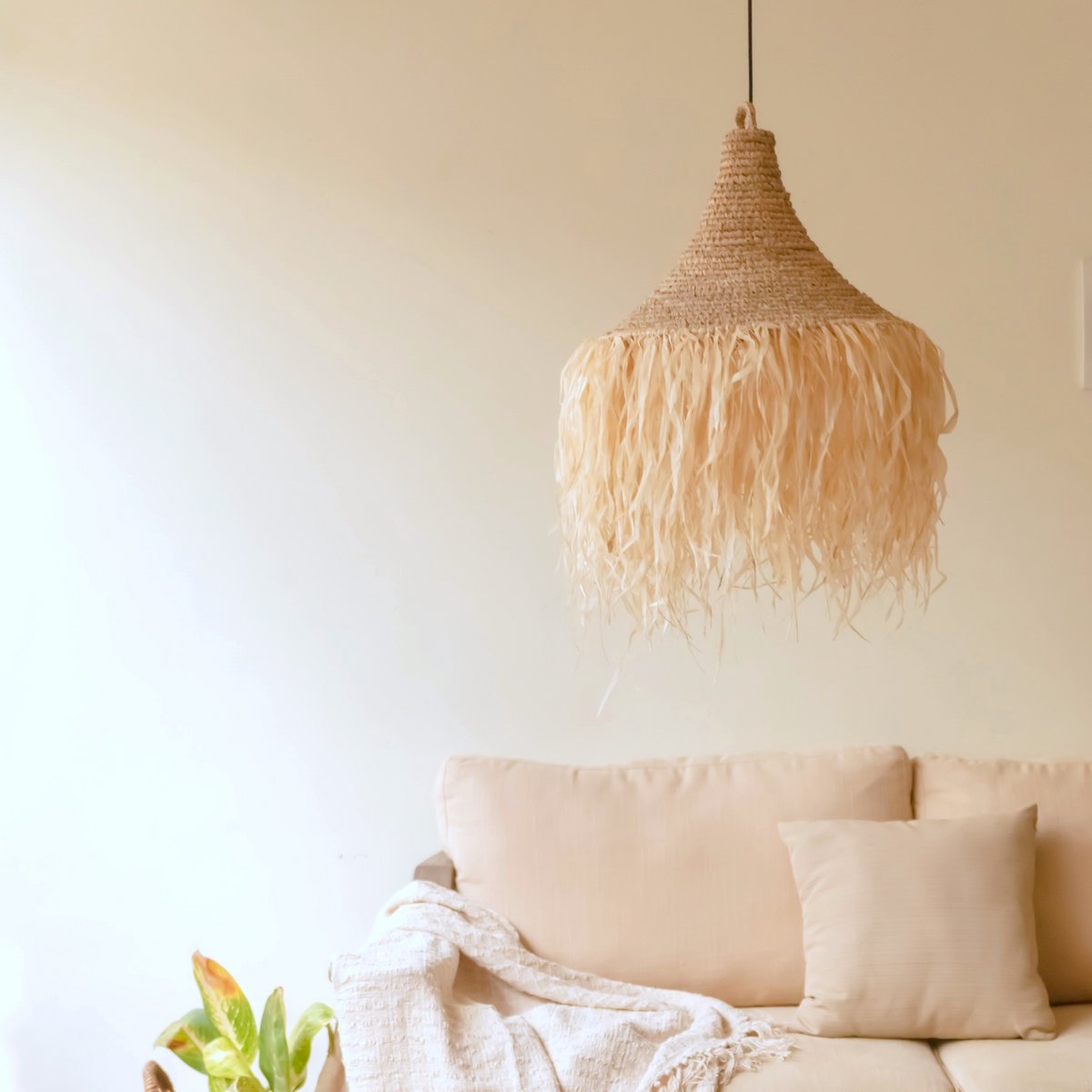 Hanglamp van raffia met franjes boven een bank voor een beige muur