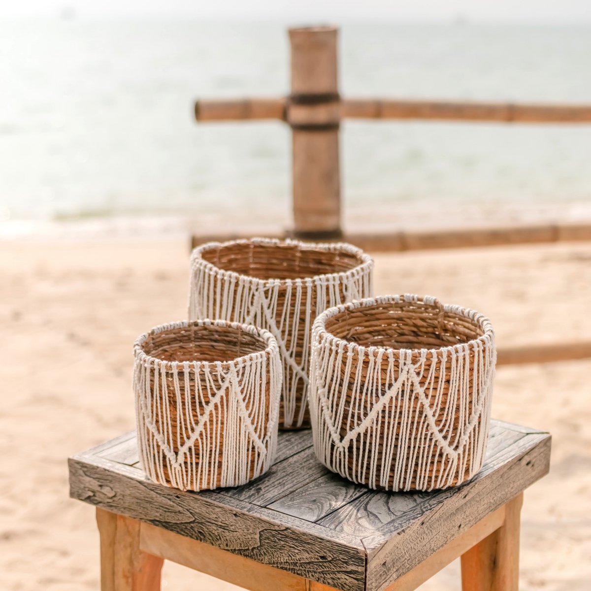 Drie macramé plantenmanden van zeegras en katoen staand op een tafeltje op het strand