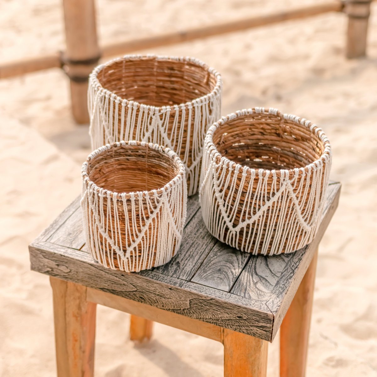 Drie macramé plantenmanden van zeegras en katoen staand op een tafeltje op het strand
