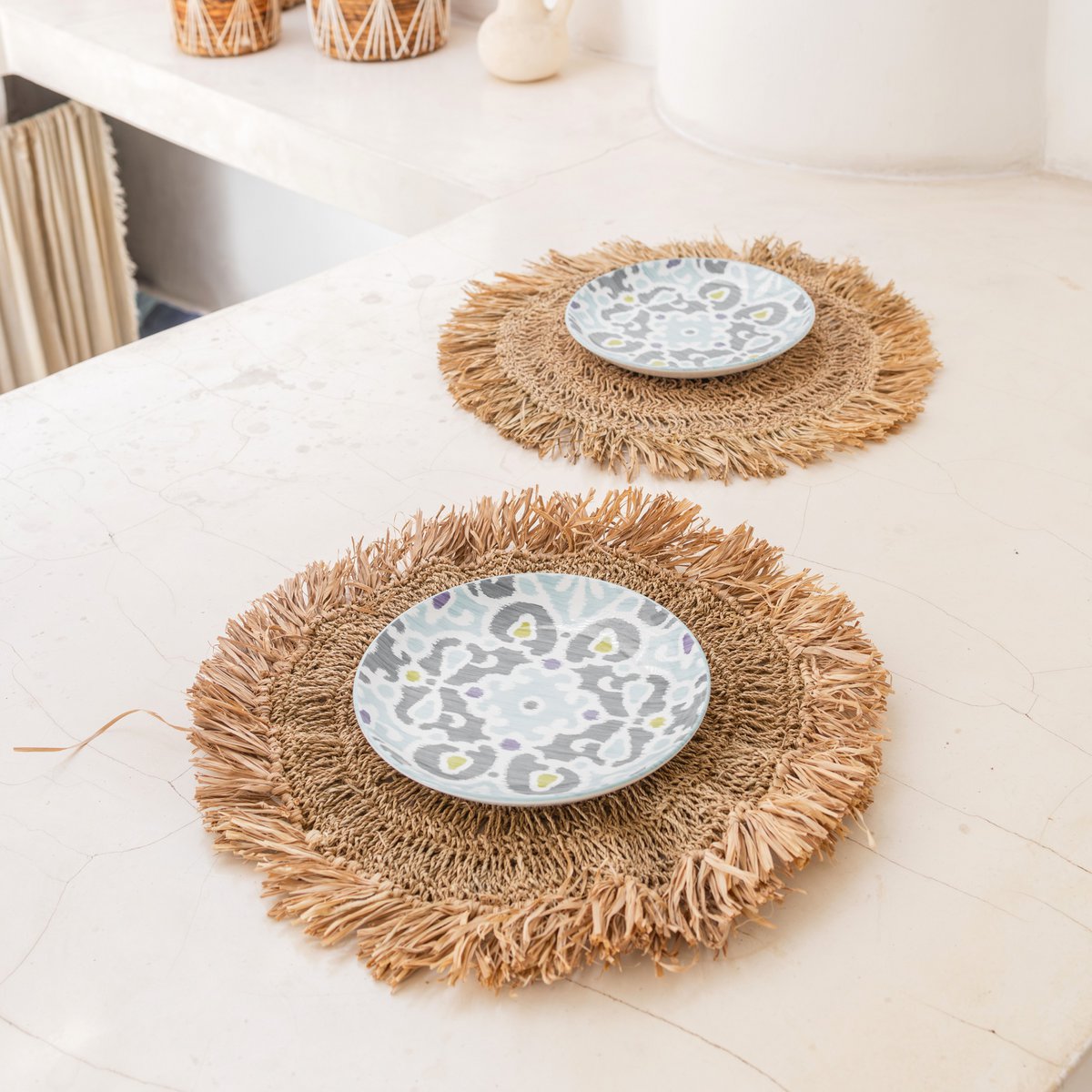 Twee placemats van raffia op een aanrecht met schoteltjes erop