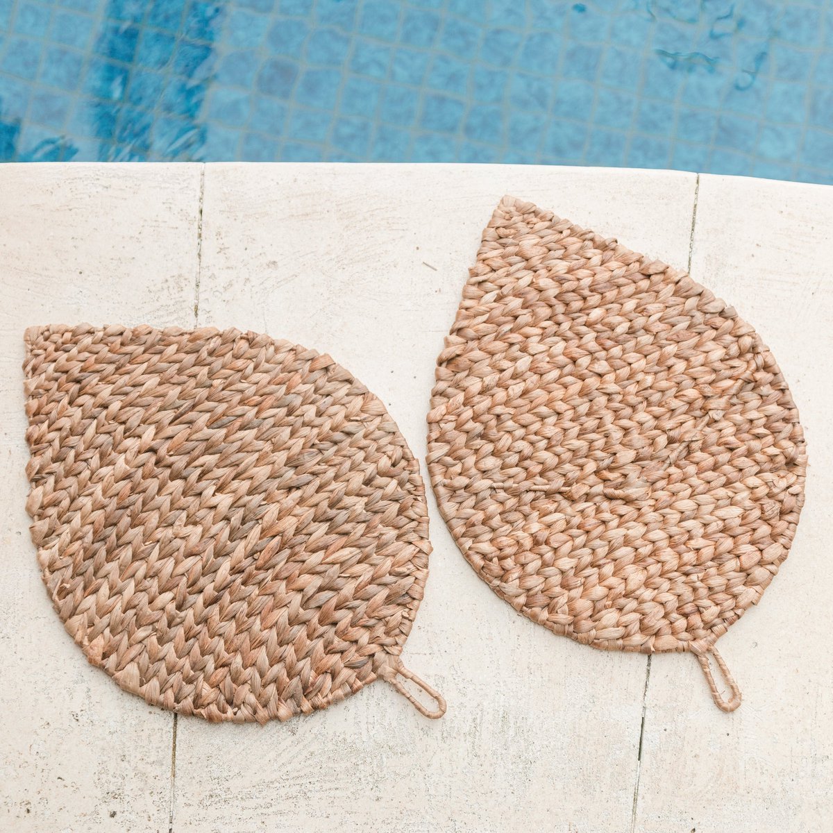 Twee placemats van waterhyacint op de grond naast een zwembad