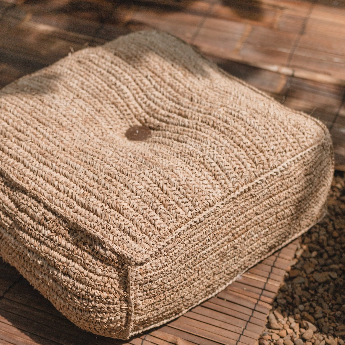 Grote vierkante poef van raffia op een houten ondergrond