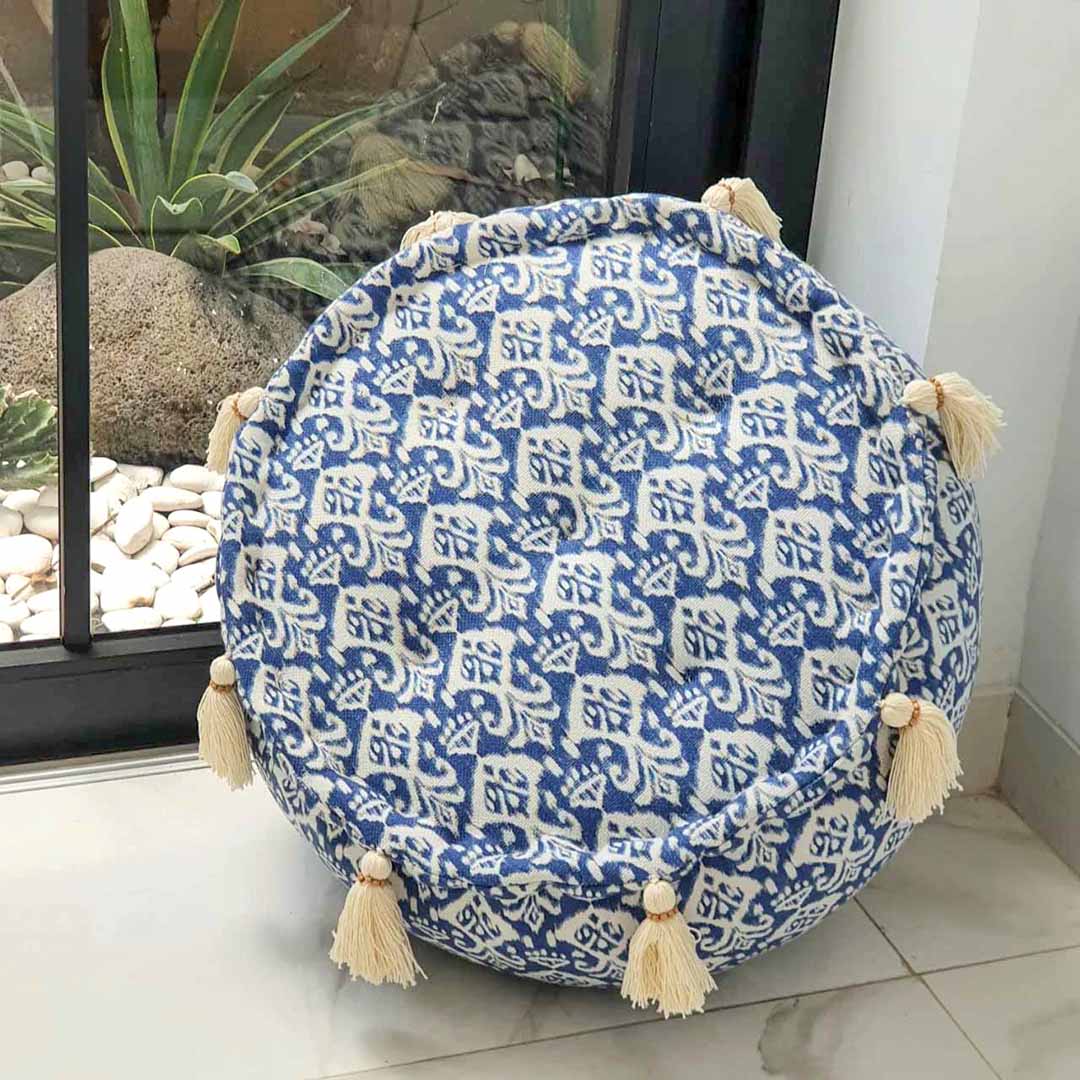 Kleine ronde blauw witte poef schuin op de zijkant staand op een beige glimmende vloer voor een raam