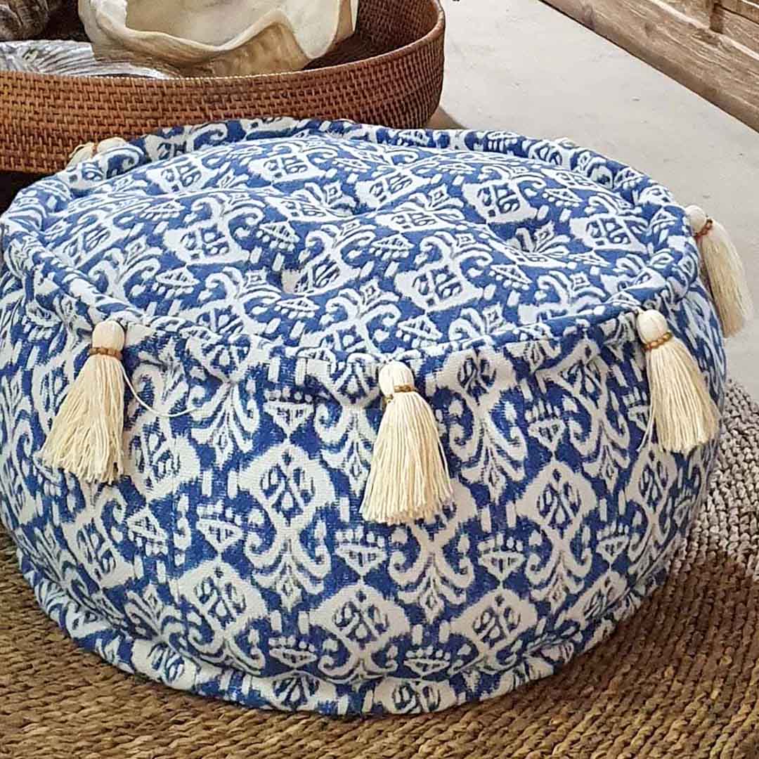 Kleine ronde blauw witte poef met witte kwastjes van dichtbij gezien, gelegen op een bruin gekleurd tapijt