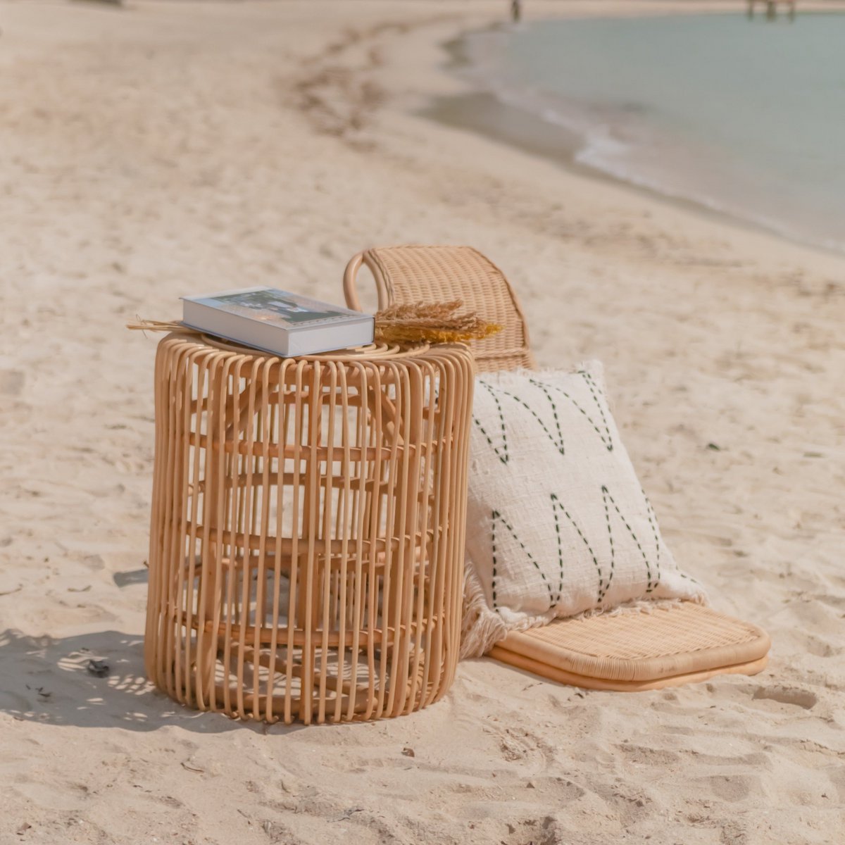 Salontafel van rotan op het strand met een kussen ernaast
