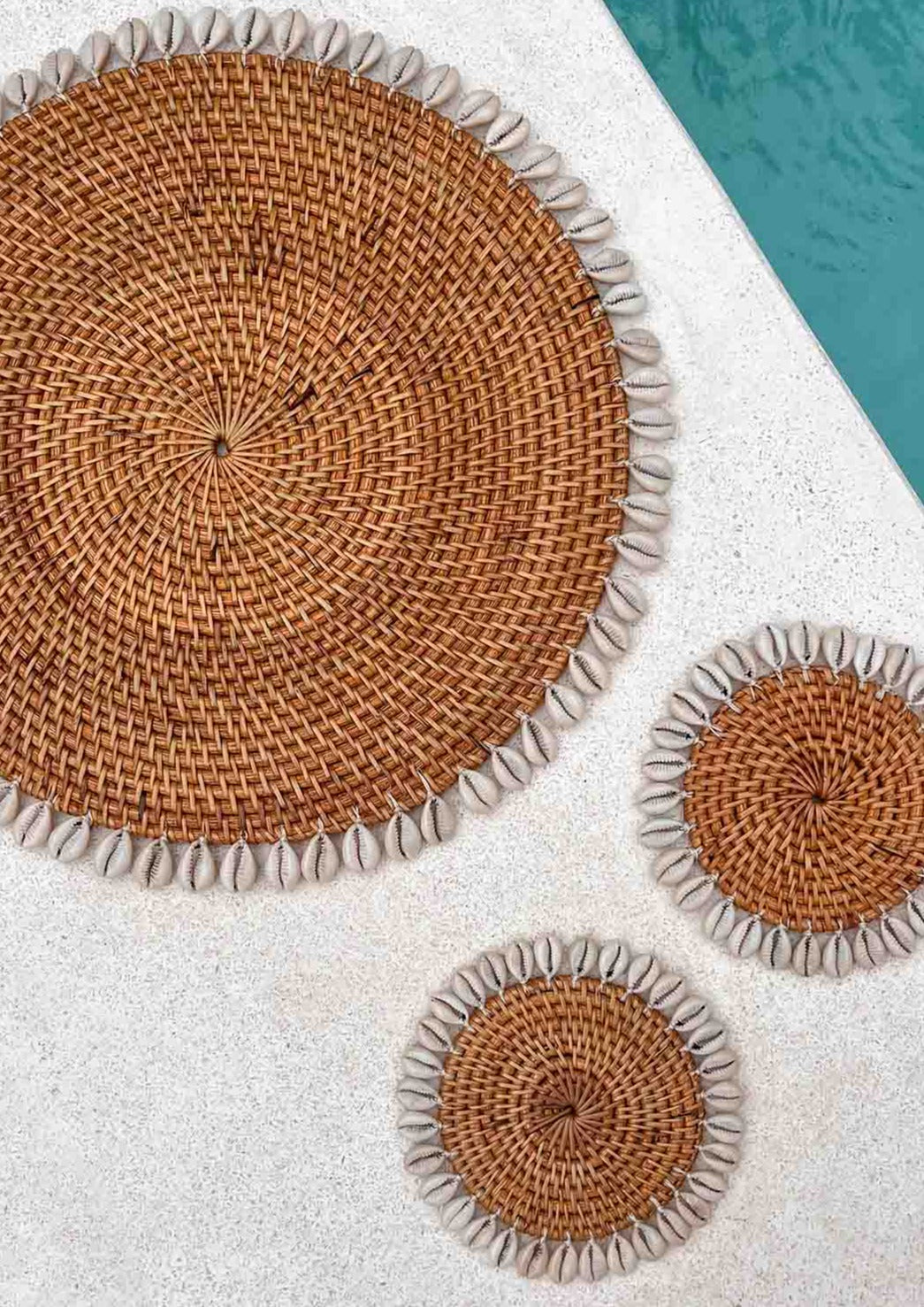 Twee schelpen onderzetters en een placemat naast een zwembad