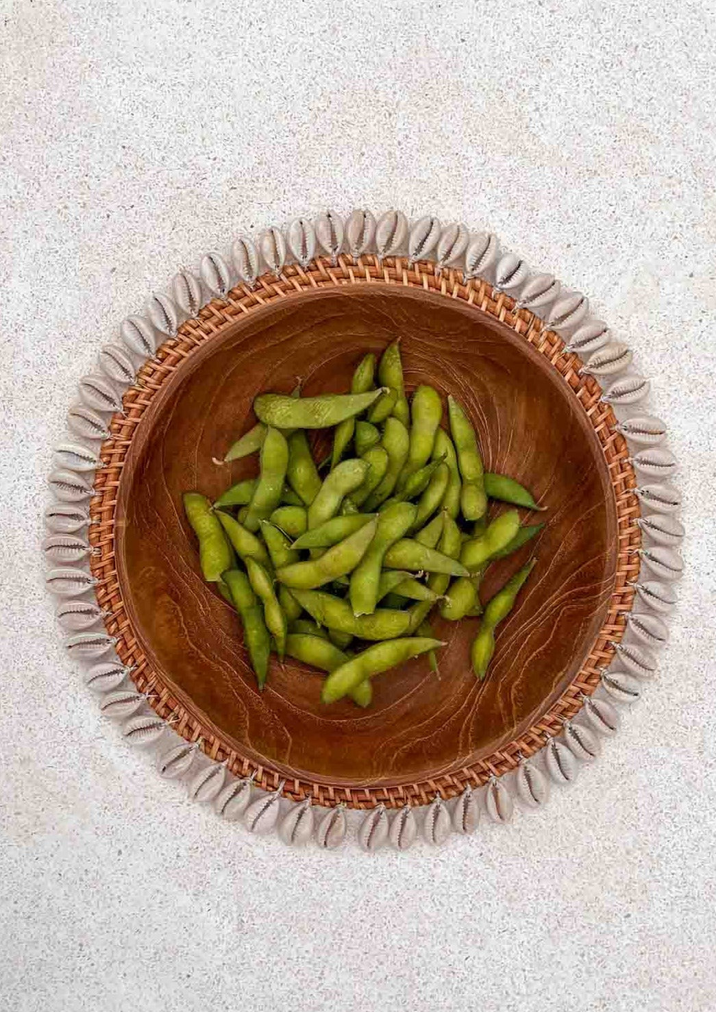Schelpen placemat met daarop een houten kom staand op de grond