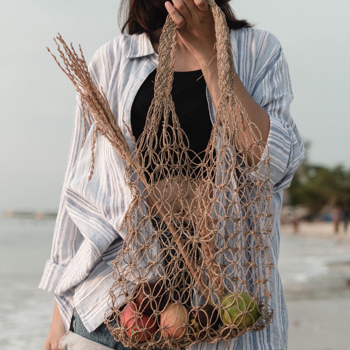 Schoudertas van raffia vastgehouden door een vrouw