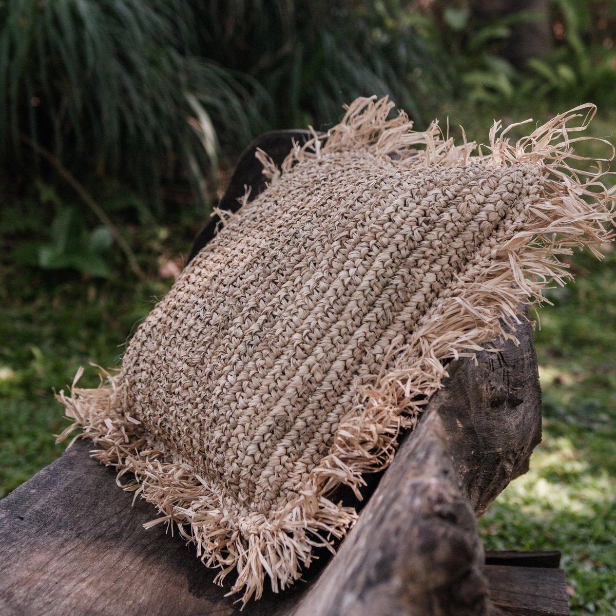 Sierkussen van raffia met franjes buiten liggend op een bankje