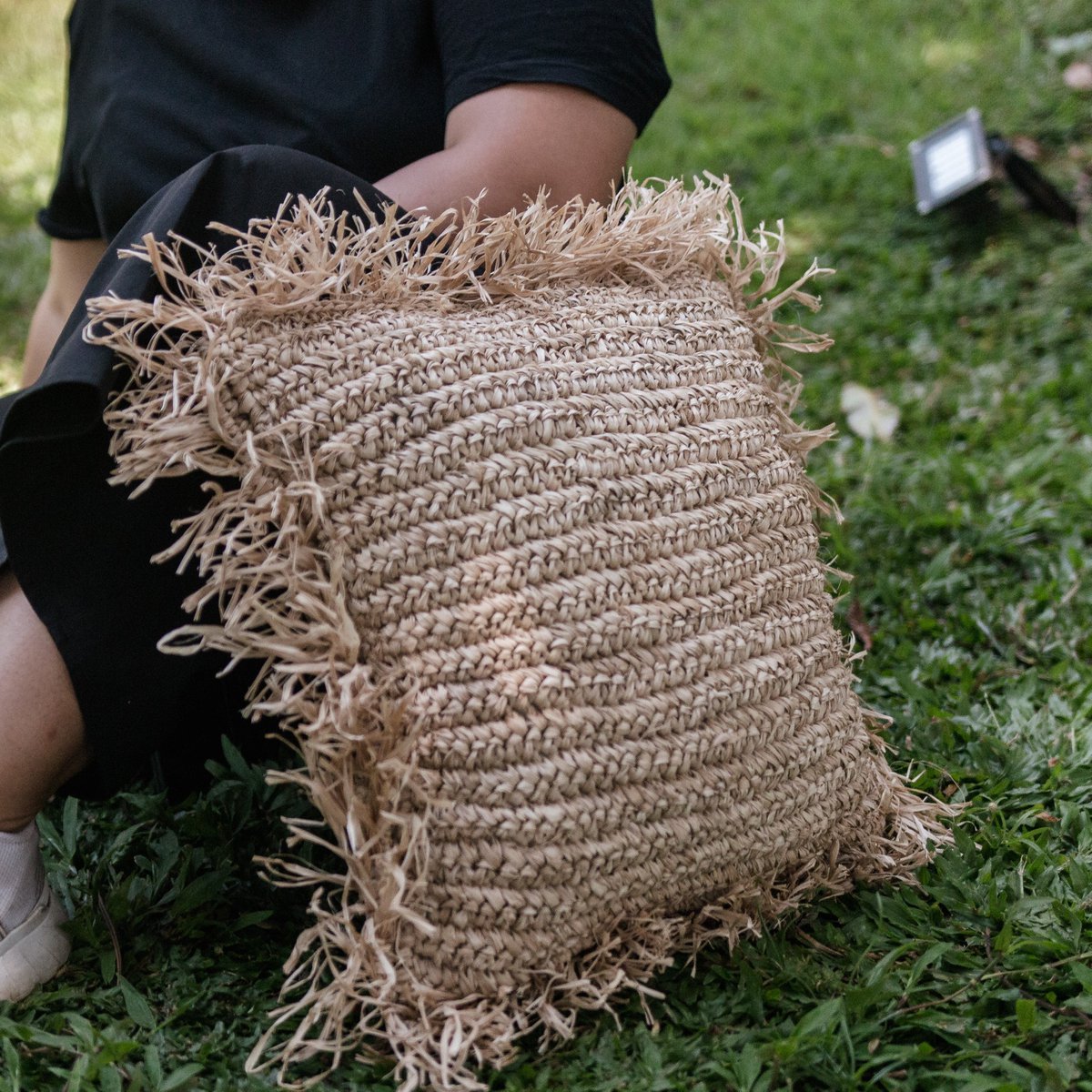 Sierkussen met vulling van raffia en franjes buiten liggend tegen een persoon aan