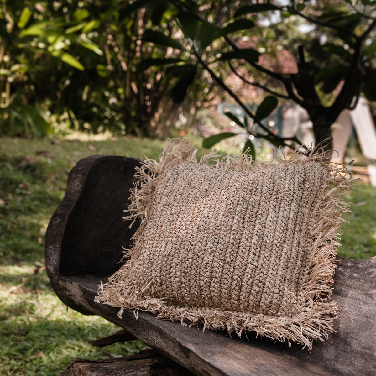 Sierkussen met vulling van raffia en franjes buiten liggend op een bankje