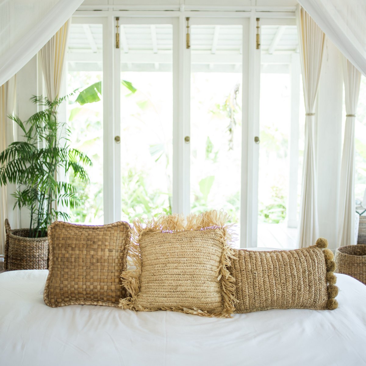 Sierkussen met vulling van raffia liggend op een bed tussen twee andere kussens