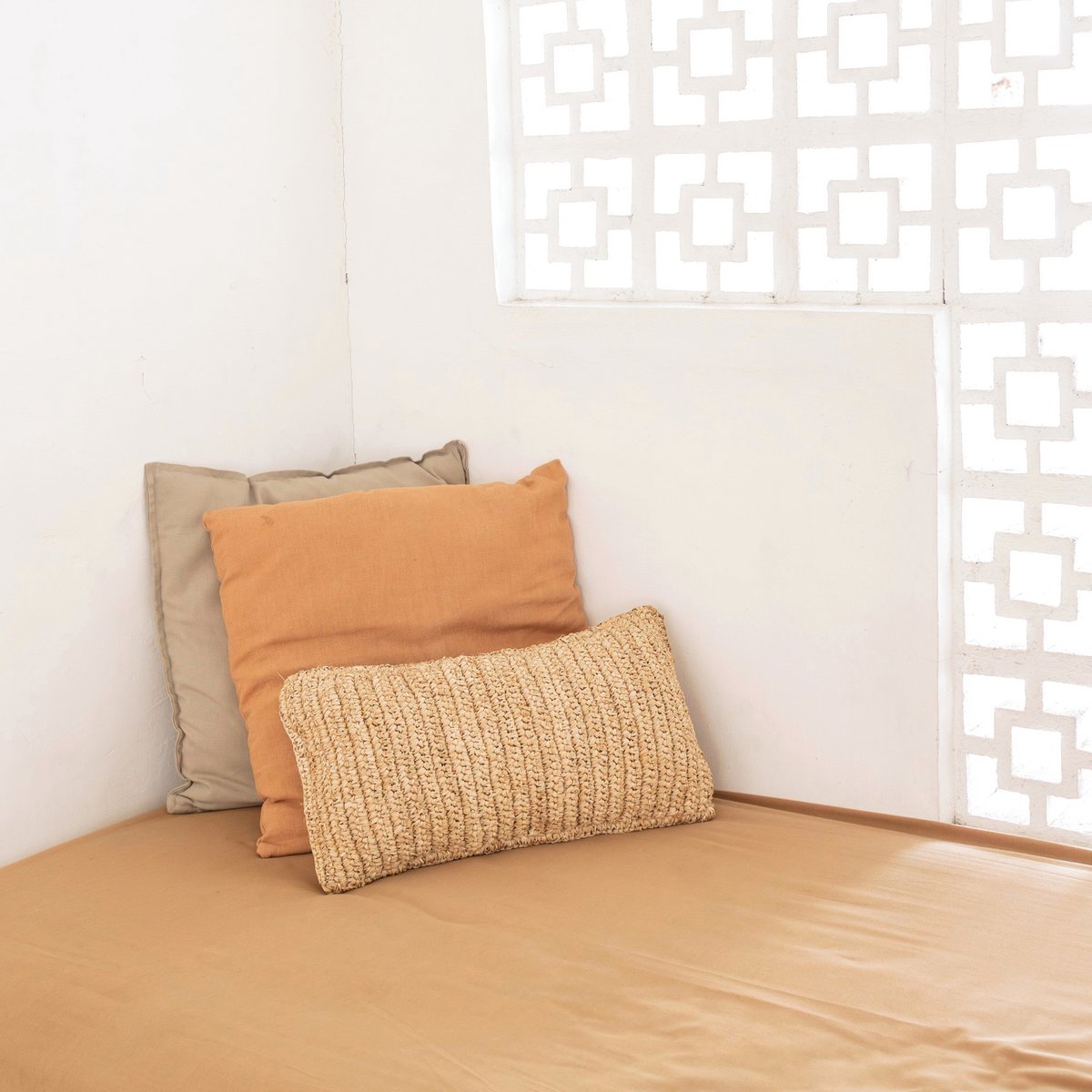 Sierkussen van raffia liggend in een hoek met twee andere kussens