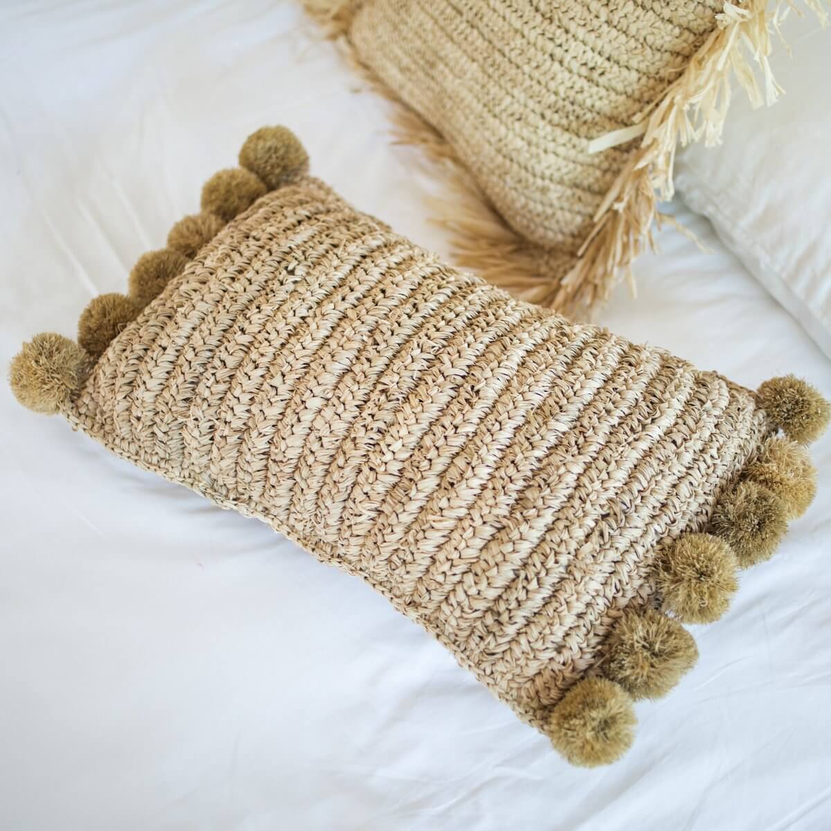 Sierkussen van raffia liggend op een witte bank