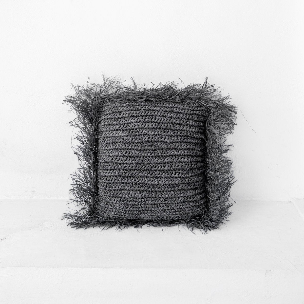 Sierkussen met vulling van raffia in de kleur zwart met franjes tegen een witte muur