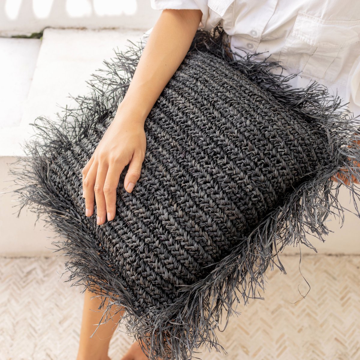 Sierkussen met vulling van raffia in de kleur zwart op de schoot van een vrouw