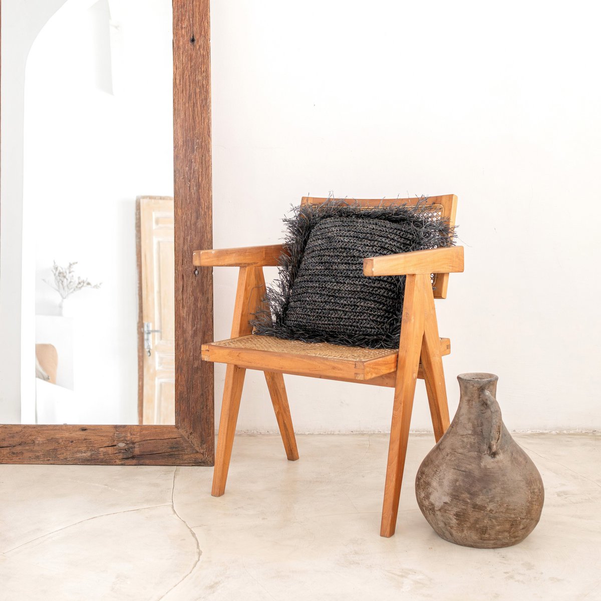 Sierkussen met vulling van raffia in de kleur zwart met franjes liggend op een stoel