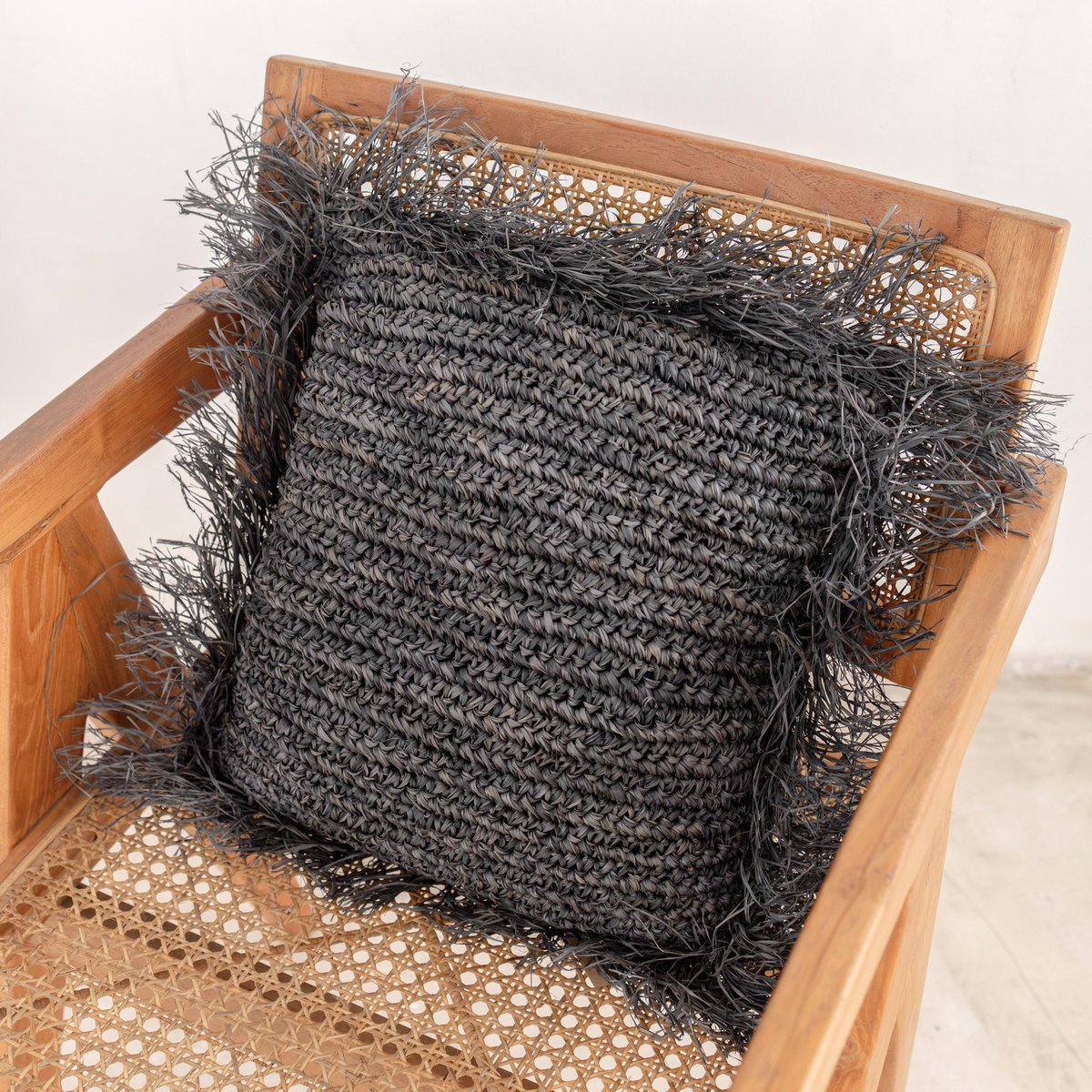 Sierkussen met een vulling van raffia in de kleur zwart met franjes liggend op een stoel