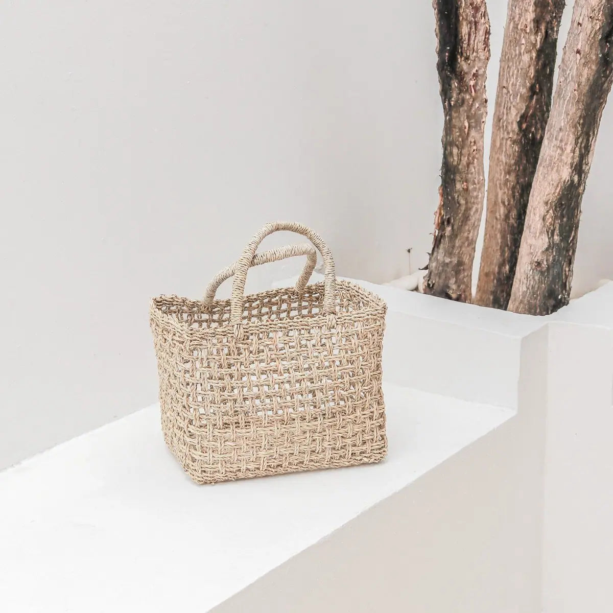 Tas van handgeweven raffia op een witte stenen ondergrond