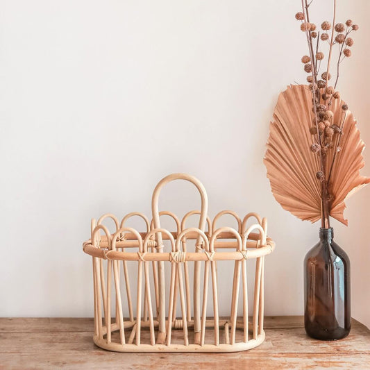 Tijdschriftenhouder van rotan staand op een houten ondergrond voor een muur