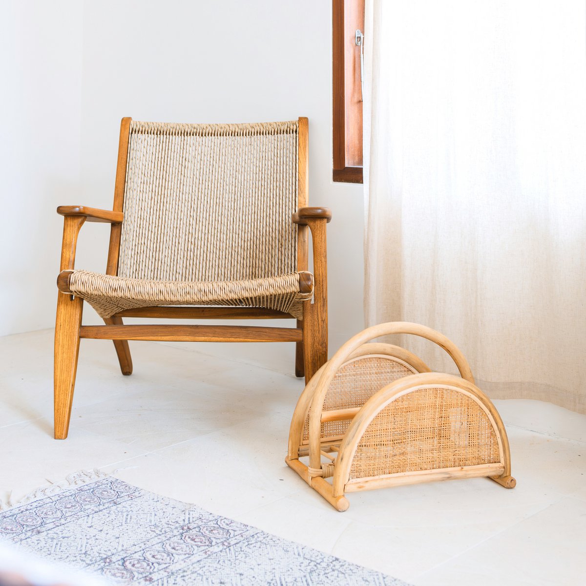 Rotan tijdschriftenmand op de vloer naast een houten stoel met rotan zitting en rugleuning, in een lichte kamer.
