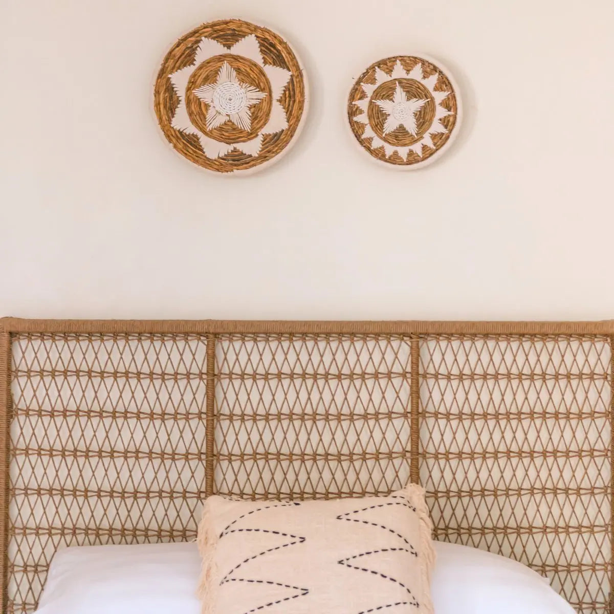 Wanddecoratie van bananenvezel hangend aan een witte muur boven een bed