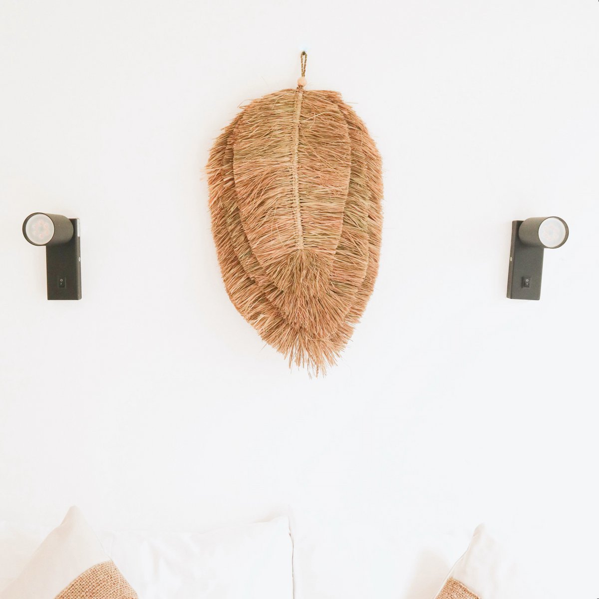 Wandhanger van handgeweven raffia boven een bed tussen twee lampen