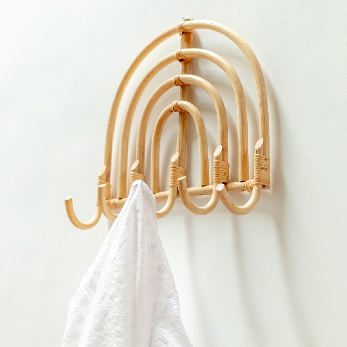 Wandhanger van rotan met een wit shirt eraan aan een witte muur van dichtbij gezien