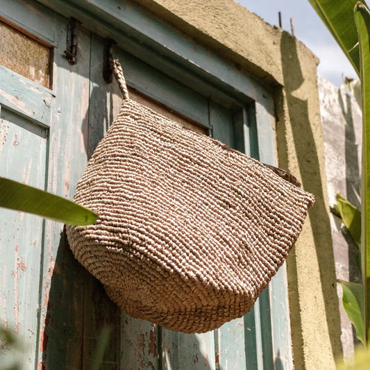 Wandmand van raffia aan een haak aan de muur hangend