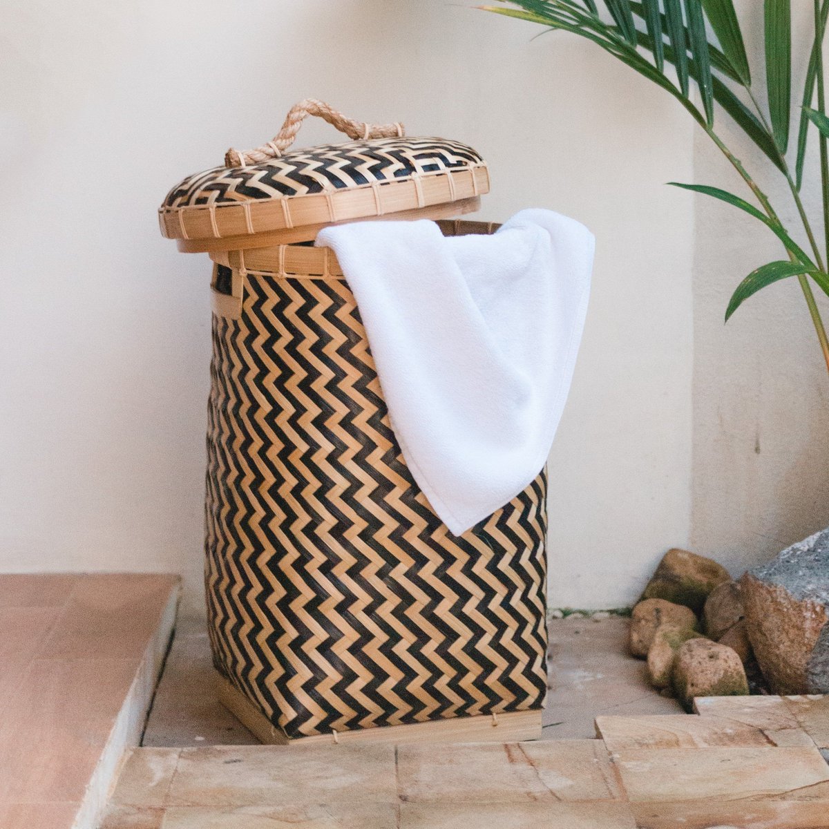 Wasmand van bamboe met deksel schuin erop met een handdoek erin voor een muur