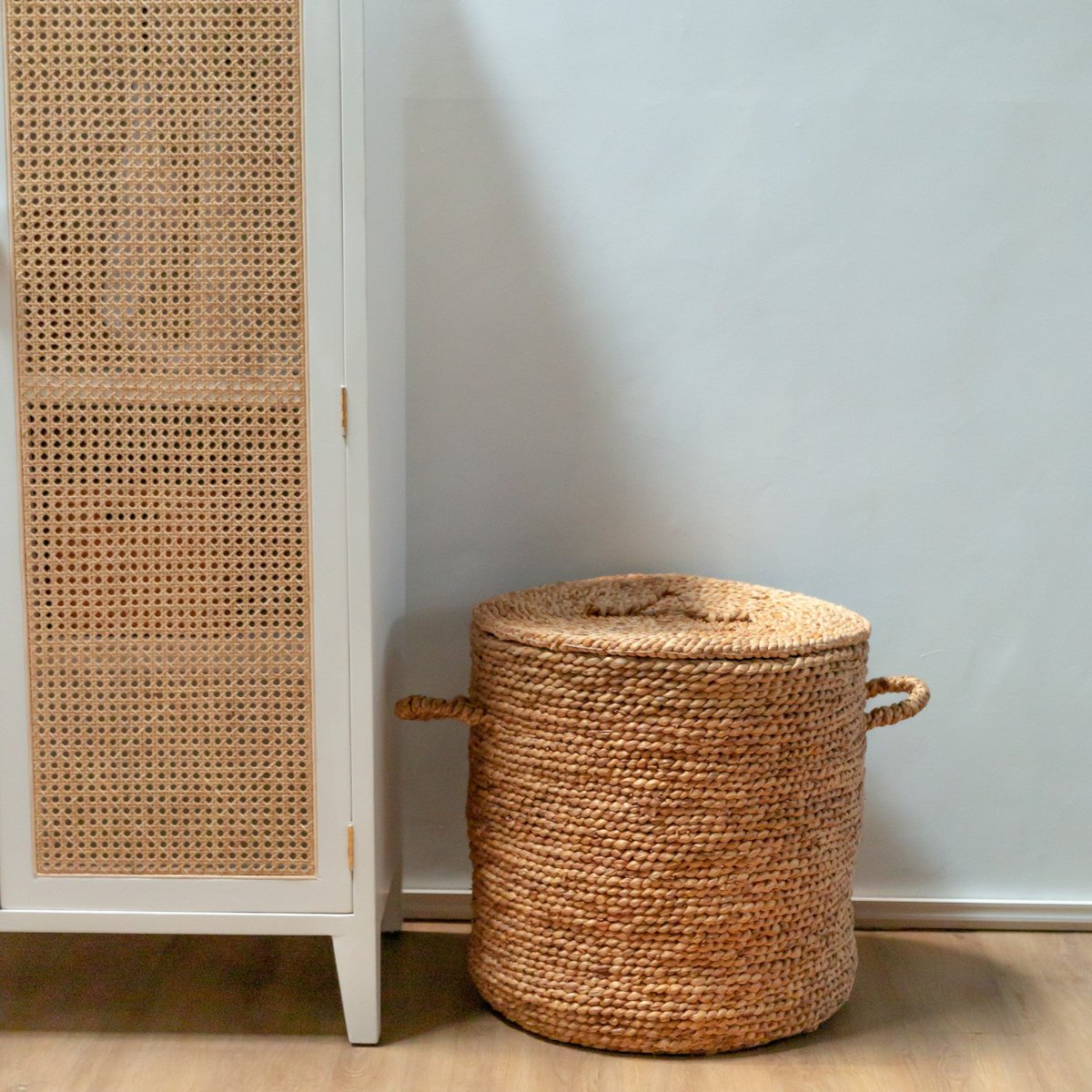 Wasmand van waterhyacint met deksel naast een kast