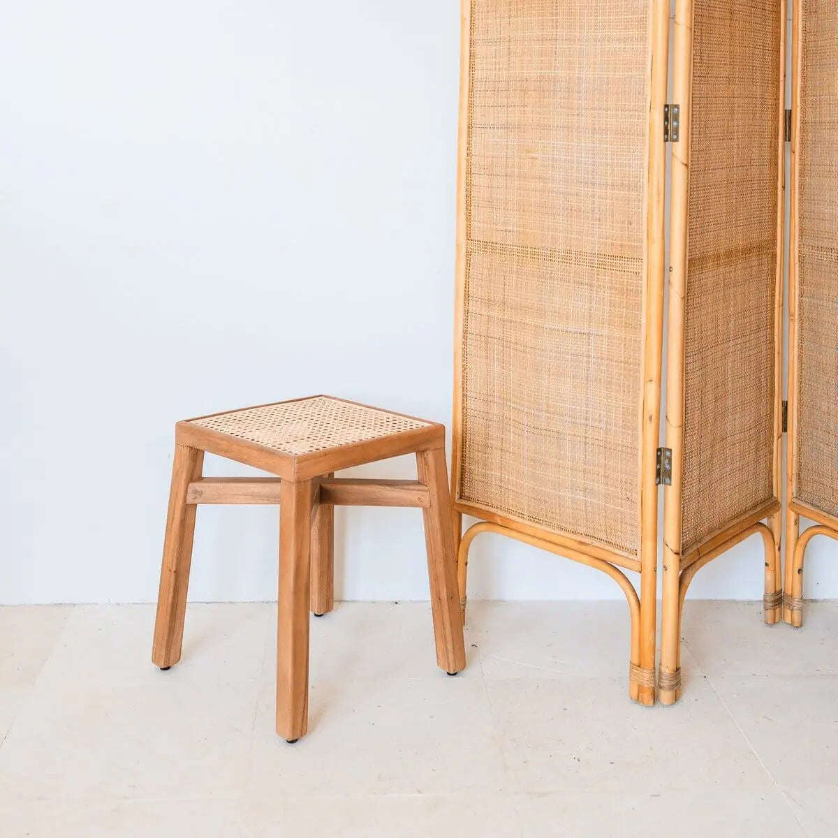 Vierkant krukje van hout in bohemian stijl staand naast een houten kamerscherm